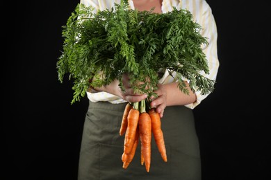 Photo of Woman holding ripe carrots on black background, closeup