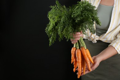 Photo of Woman holding ripe carrots on black background, closeup. Space for text