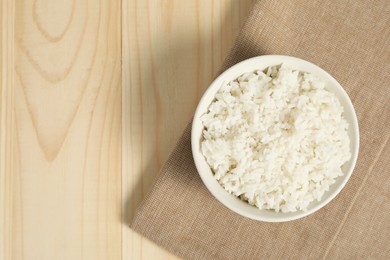 Photo of Delicious boiled rice in bowl on wooden table, top view. Space for text