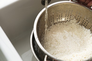 Pouring water into colander with rice in sink, closeup