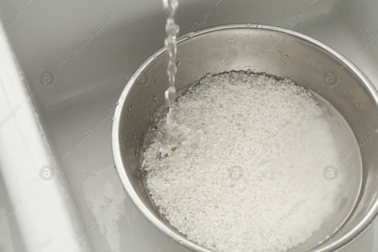 Photo of Pouring water into bowl with rice in sink, closeup