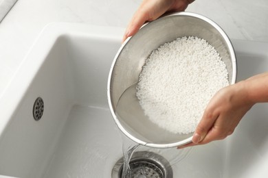 Photo of Woman rinsing rice in bowl above sink, closeup