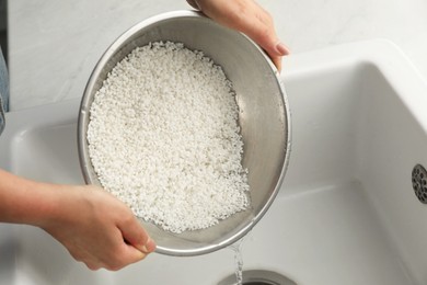 Woman rinsing rice in bowl above sink, closeup