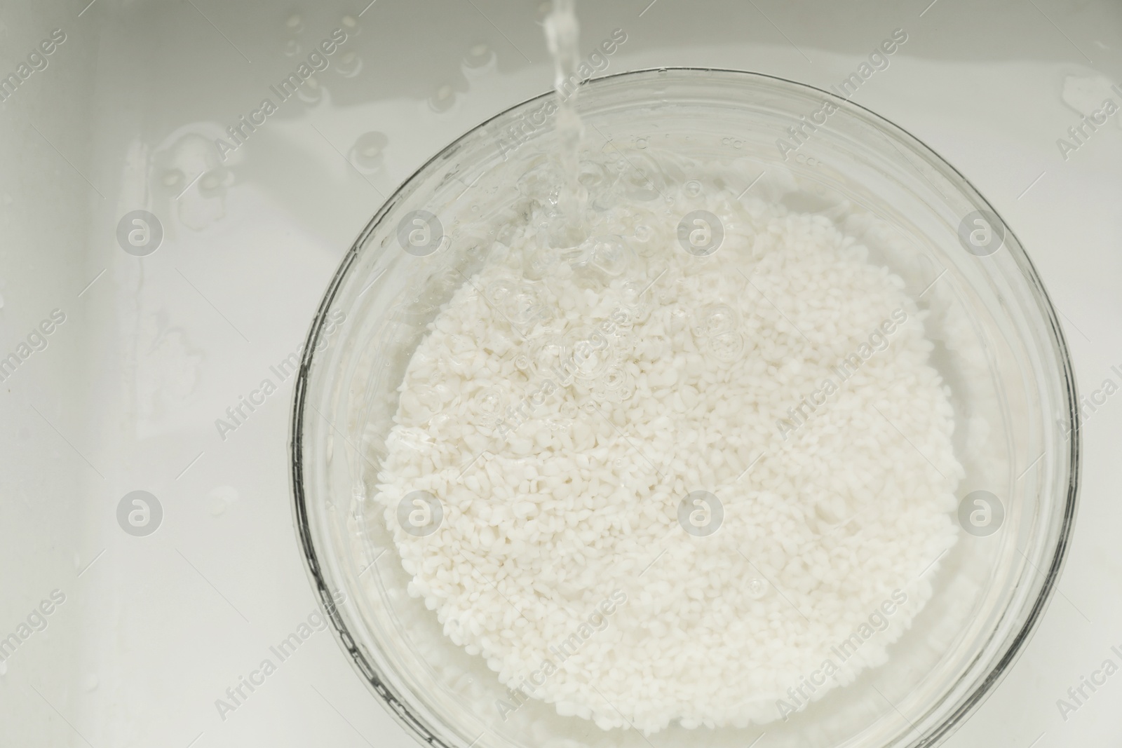 Photo of Pouring water into bowl with rice in sink, top view