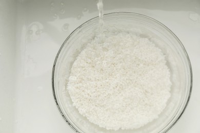 Photo of Pouring water into bowl with rice in sink, top view