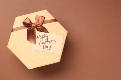 Photo of Card with phrase Happy Father's Day and gift box on light brown background, top view. Space for text