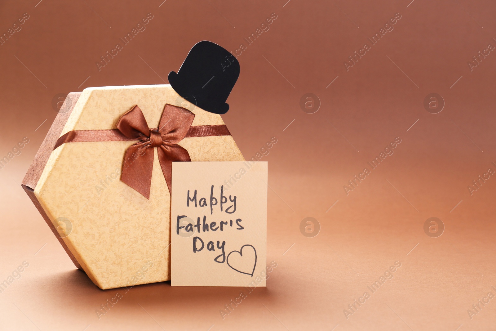 Photo of Card with phrase Happy Father's Day, hat and gift box on light brown background, space for text