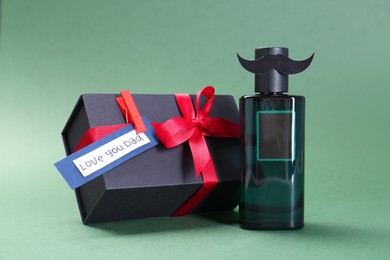 Photo of Happy Father's Day. Bottle of product with moustache, phrase Love You Dad and gift box on green background