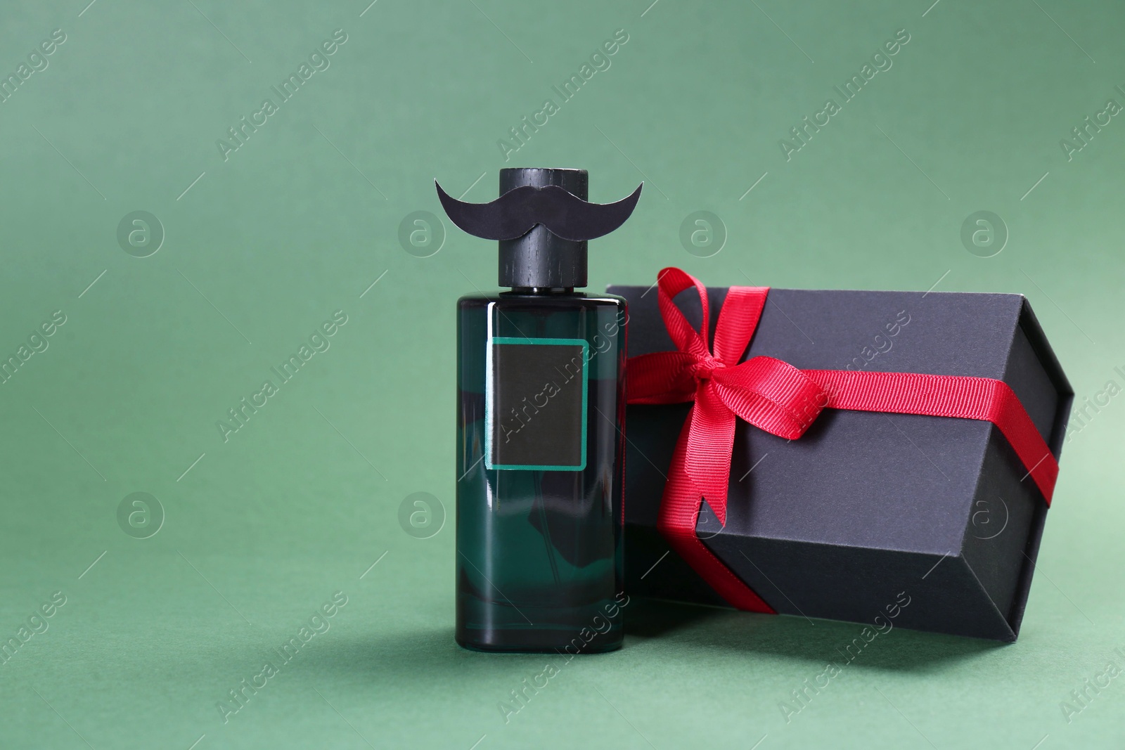 Photo of Happy Father's Day. Bottle of product with moustache and gift box on green background, space for text