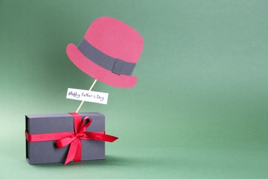 Photo of Phrase Happy Father's Day, gift box and paper hat on green background, space for text