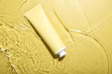 Photo of Tube with cream in water on yellow background, top view. Cosmetic product