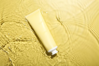 Photo of Tube with cream in water on yellow background, top view. Cosmetic product