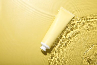 Photo of Tube with cream in water on yellow background, top view. Cosmetic product