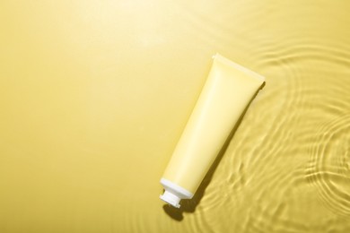 Photo of Cosmetic product. Tube with cream in water on yellow background, top view. Space for text