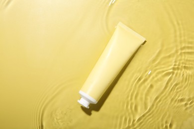 Photo of Cosmetic product. Tube with cream in water on yellow background, top view. Space for text