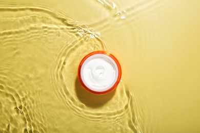 Photo of Jar with cream in water on yellow background, top view. Cosmetic product