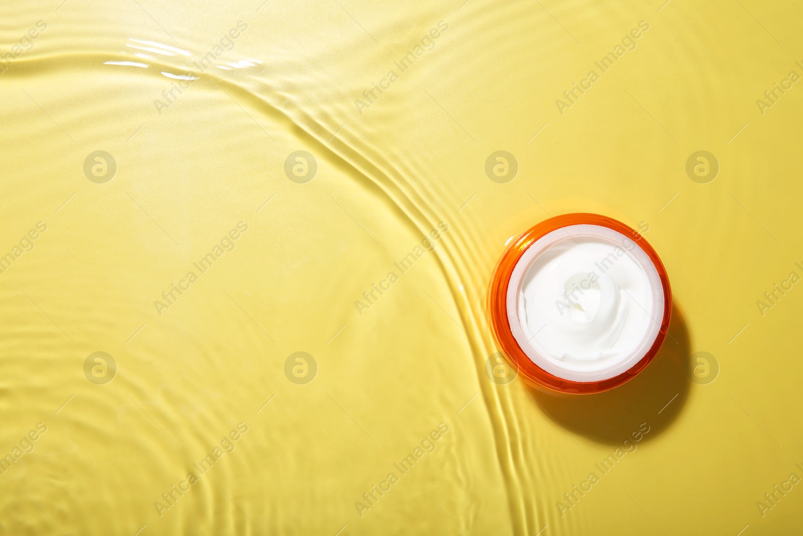 Photo of Cosmetic product. Jar with cream in water on yellow background, top view. Space for text