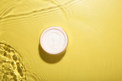 Photo of Jar with cream in water on yellow background, top view. Cosmetic product