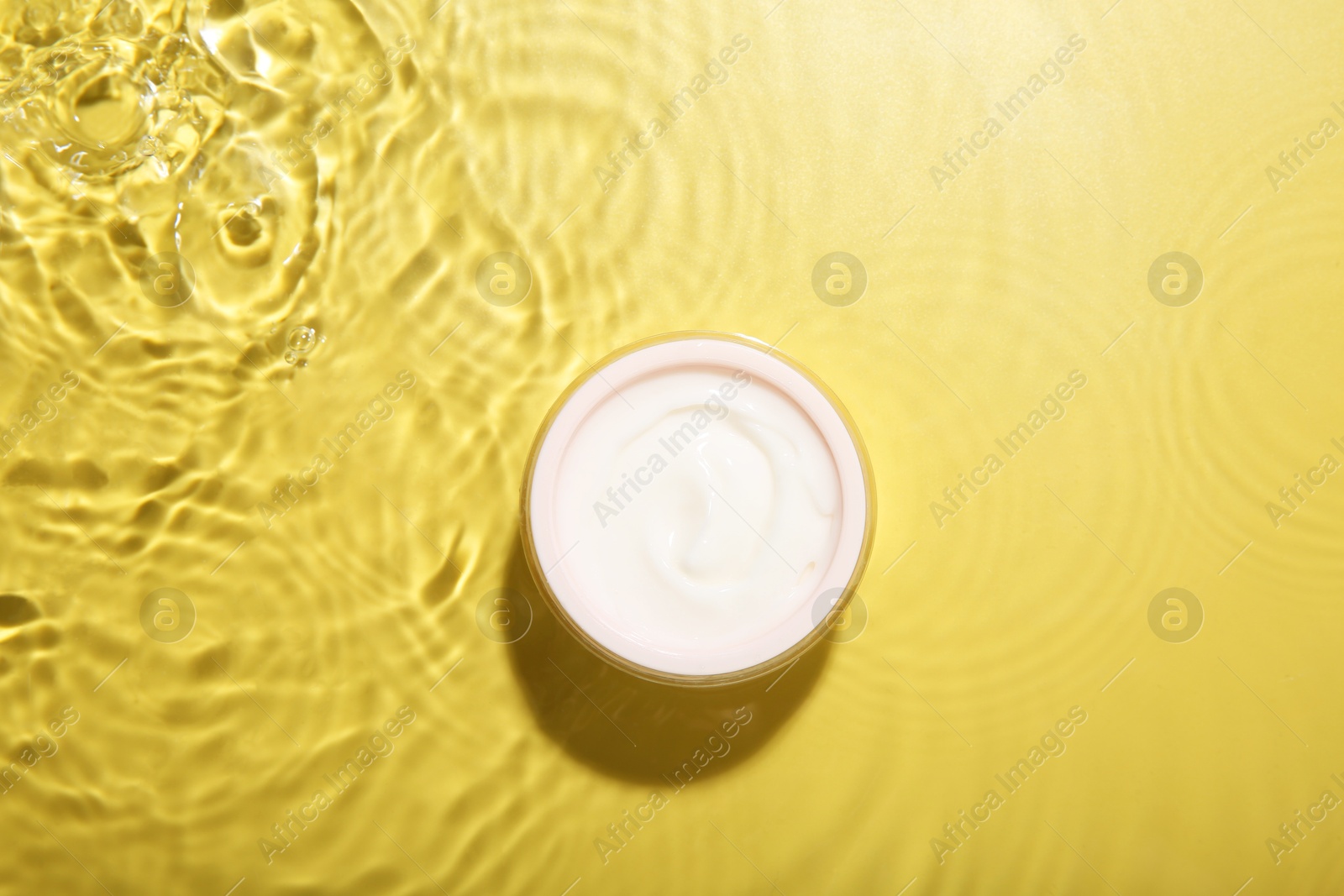 Photo of Jar with cream in water on yellow background, top view. Cosmetic product