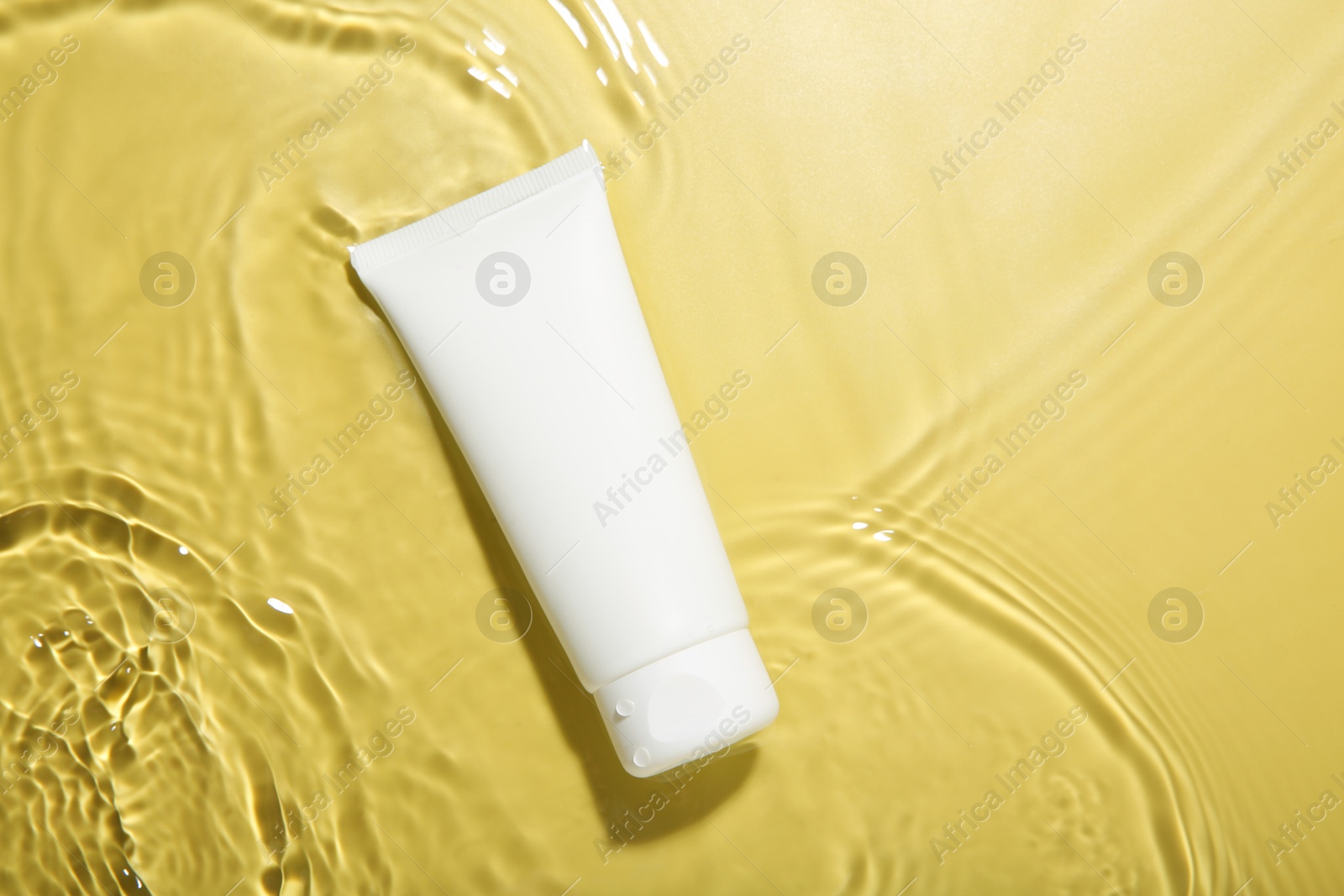 Photo of Tube with cream in water on yellow background, top view. Cosmetic product