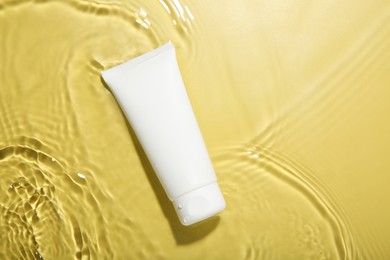 Photo of Tube with cream in water on yellow background, top view. Cosmetic product