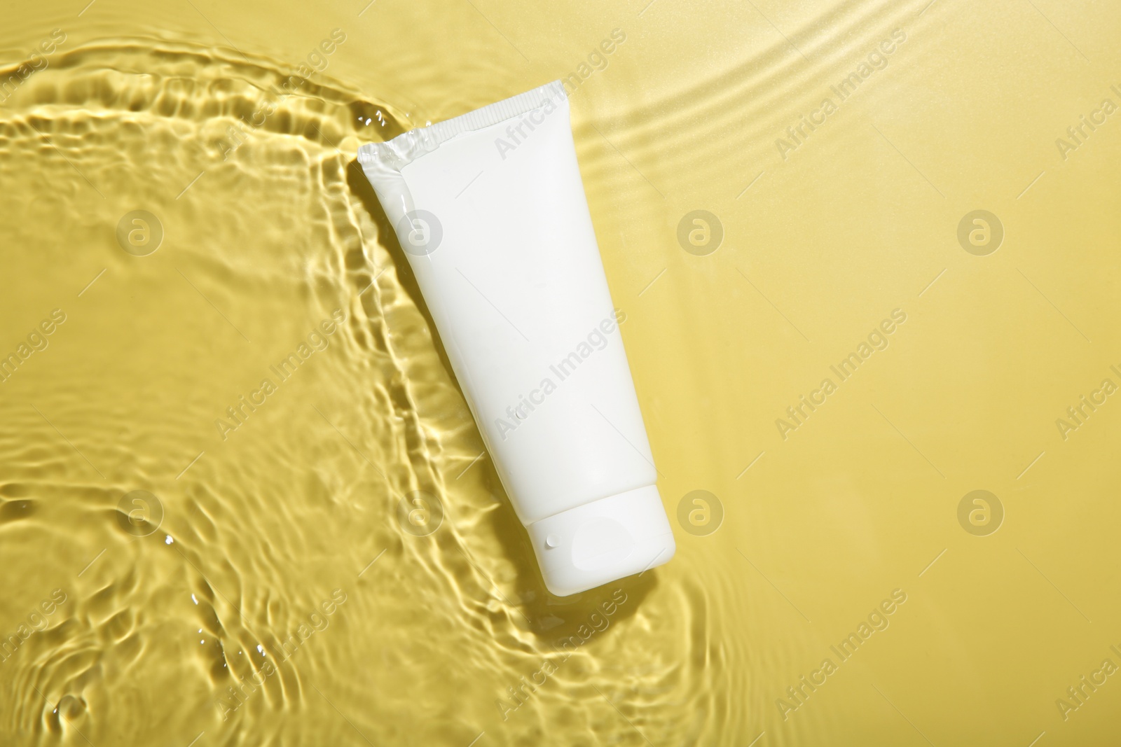 Photo of Tube with cream in water on yellow background, top view. Cosmetic product