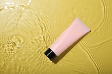 Photo of Tube with cream in water on yellow background, top view. Cosmetic product