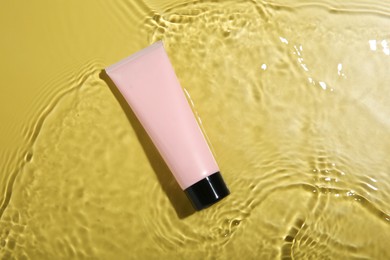 Photo of Tube with cream in water on yellow background, top view. Cosmetic product