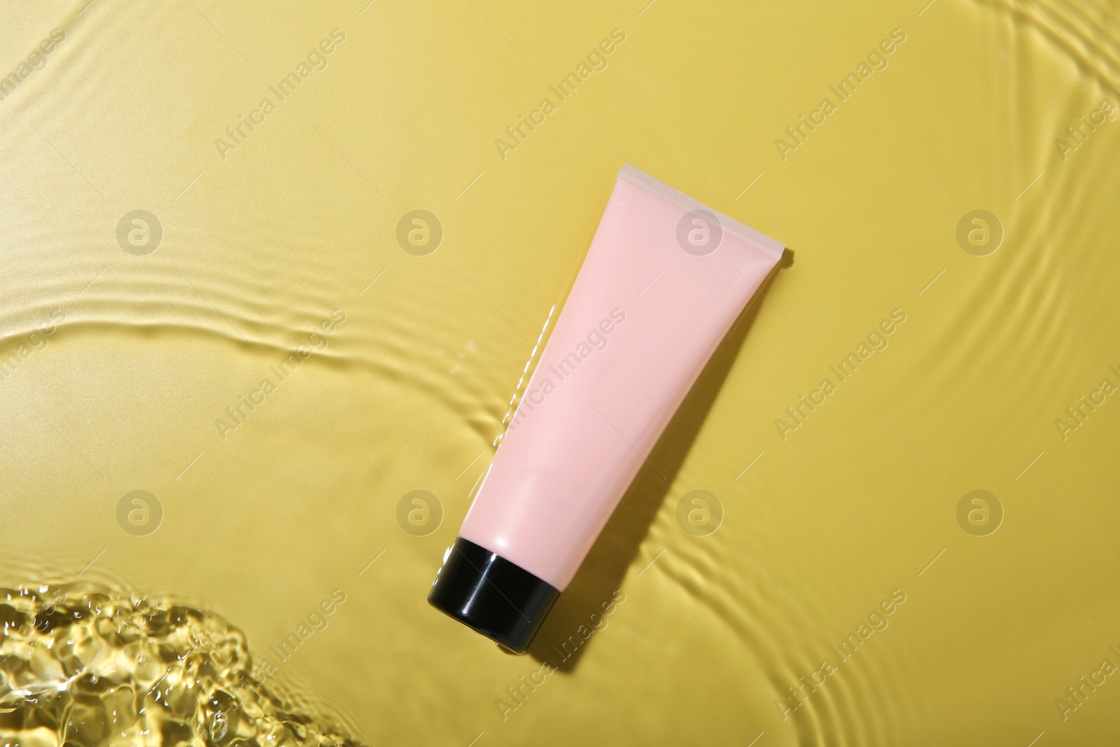 Photo of Tube with cream in water on yellow background, top view. Cosmetic product