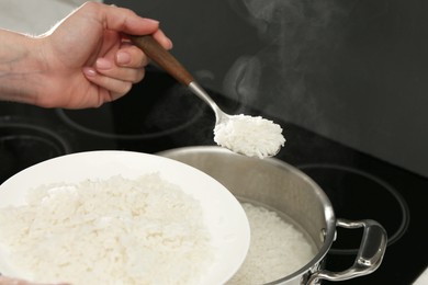 Photo of Woman taking boiled rice from pot into plate, closeup