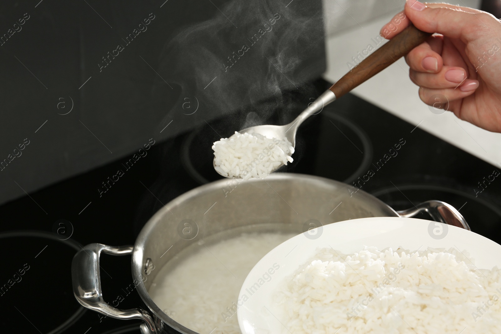 Photo of Woman taking boiled rice from pot into plate, closeup