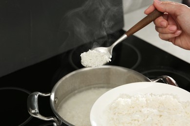 Woman taking boiled rice from pot into plate, closeup