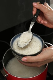 Photo of Woman taking boiled rice from pot into bowl, closeup