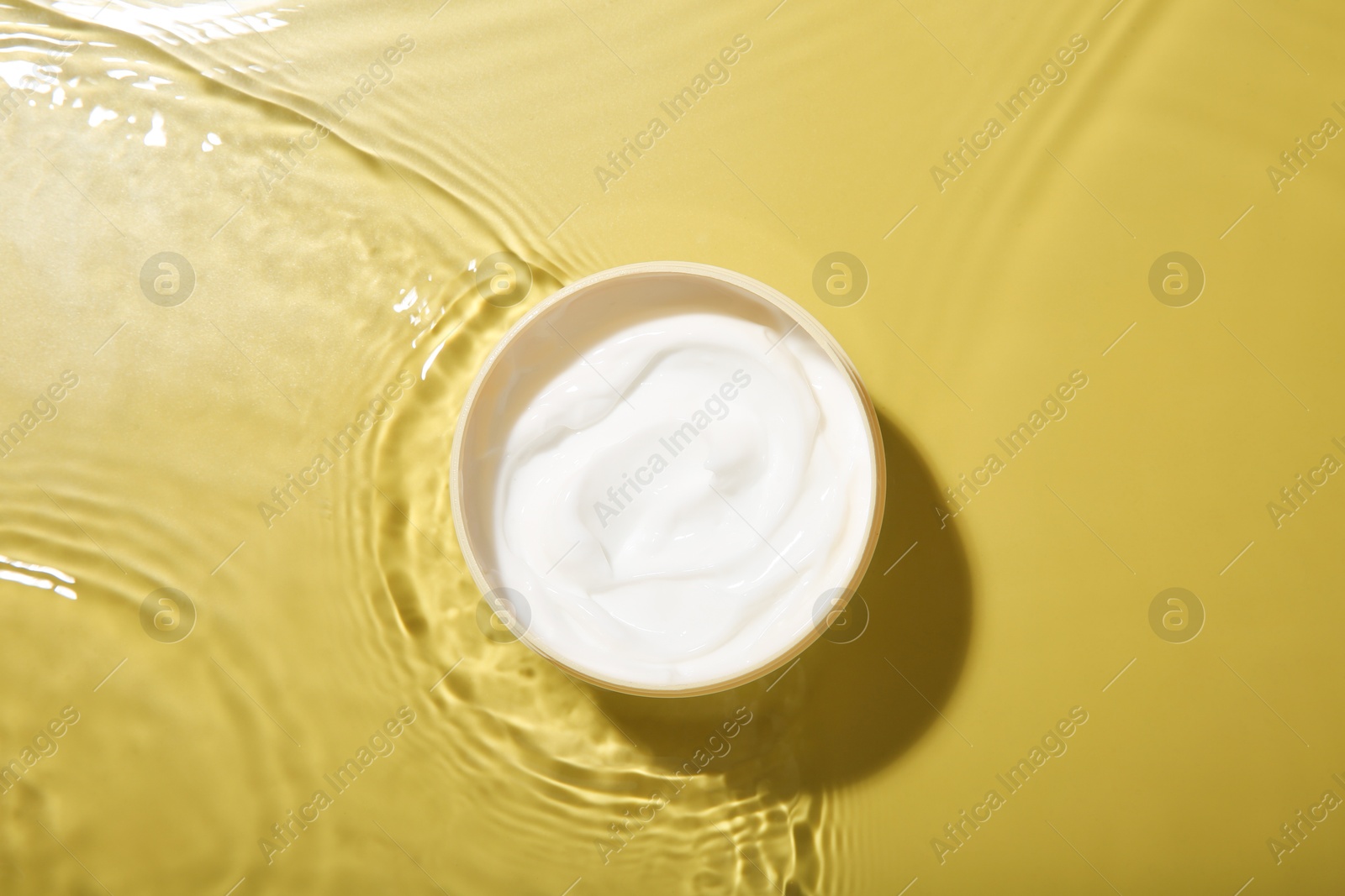 Photo of Jar with cream in water on yellow background, top view. Cosmetic product