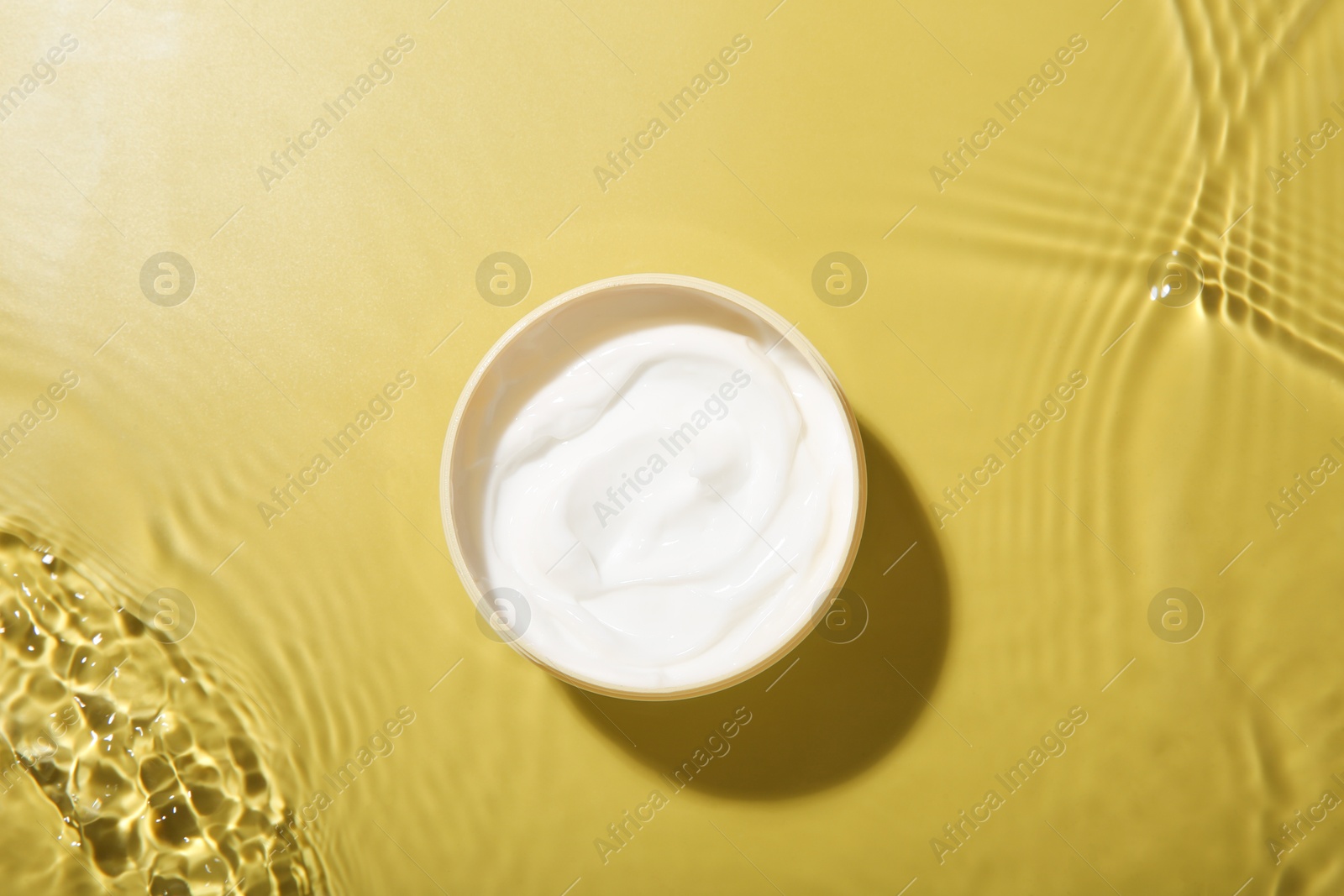 Photo of Jar with cream in water on yellow background, top view. Cosmetic product