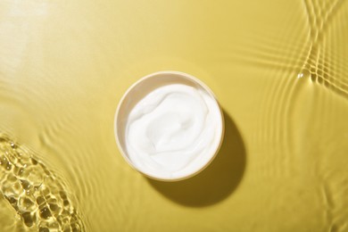 Jar with cream in water on yellow background, top view. Cosmetic product