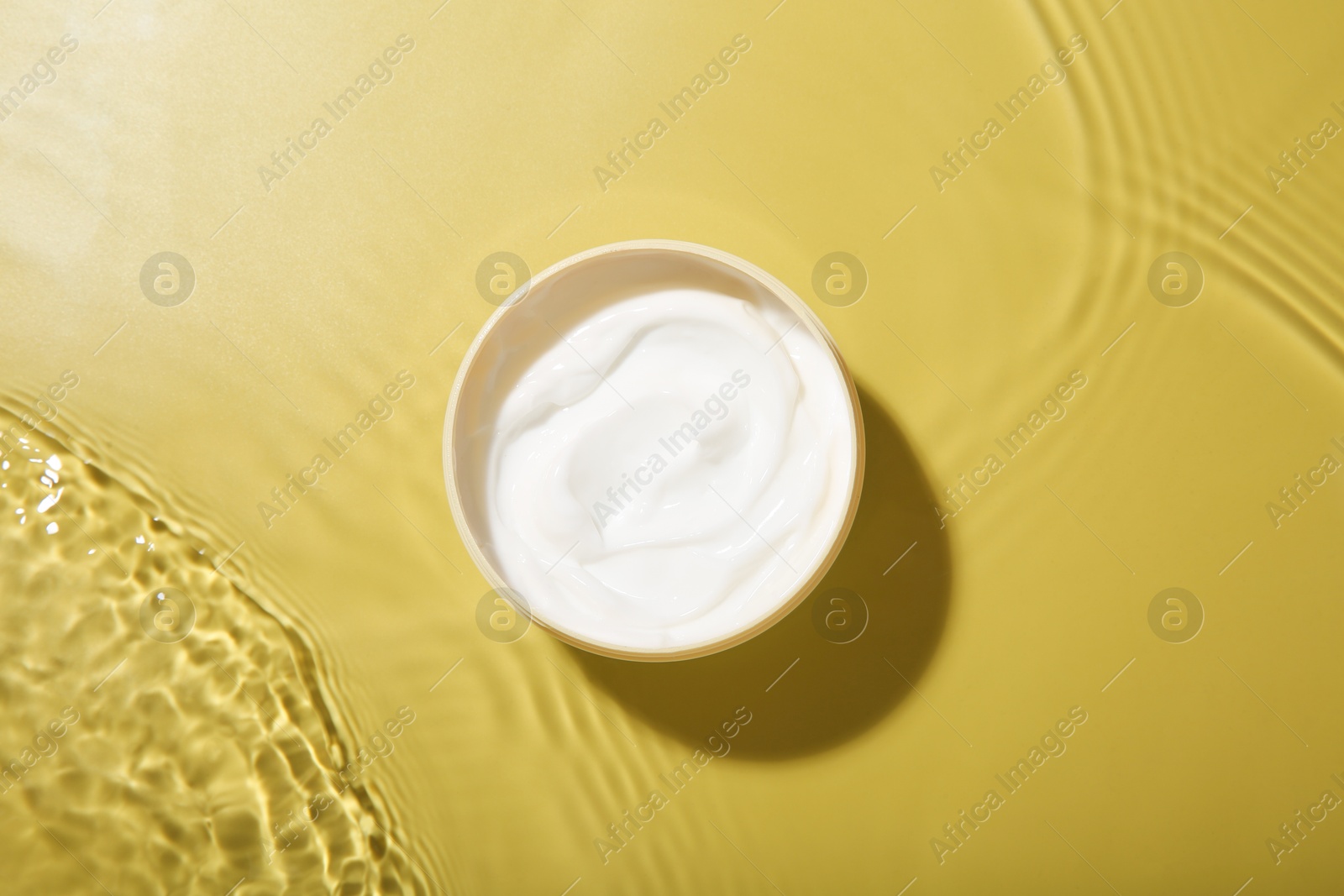 Photo of Jar with cream in water on yellow background, top view. Cosmetic product