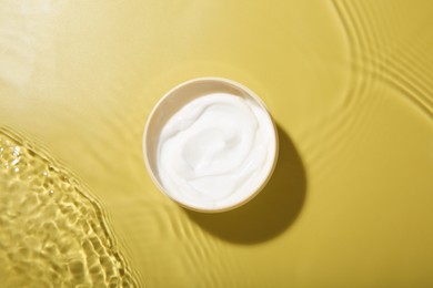 Jar with cream in water on yellow background, top view. Cosmetic product