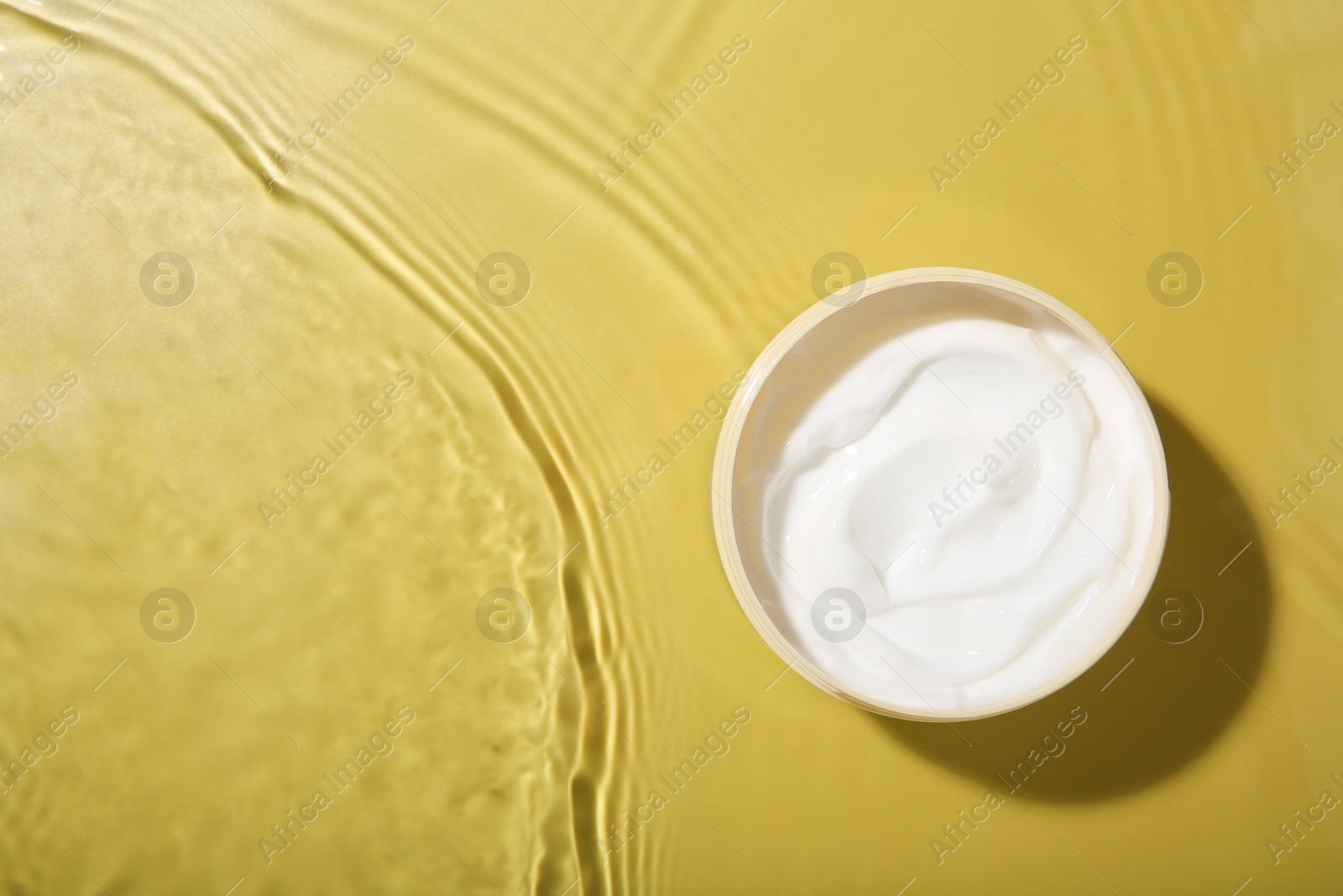 Photo of Cosmetic product. Jar with cream in water on yellow background, top view. Space for text