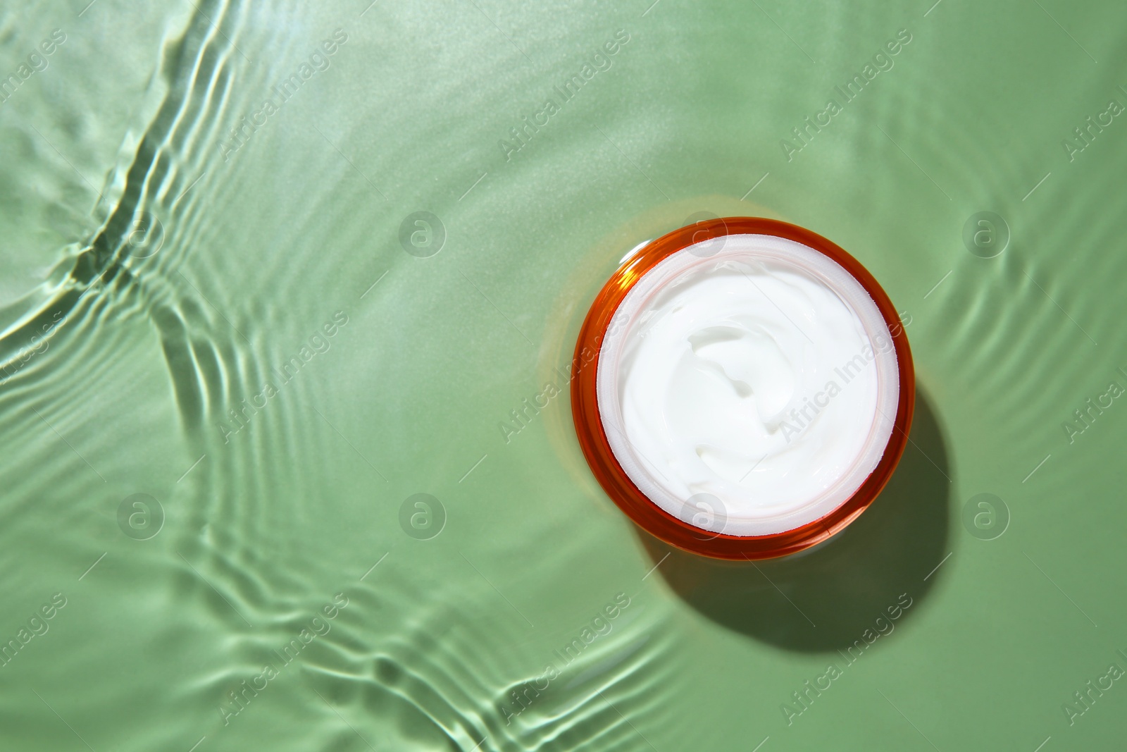 Photo of Cosmetic product. Jar with cream in water on light green background, top view. Space for text