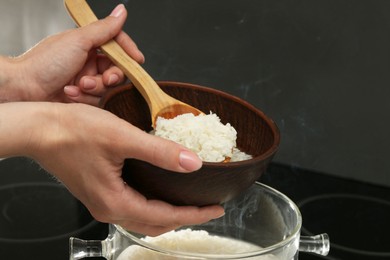 Photo of Woman taking boiled rice into bowl, closeup