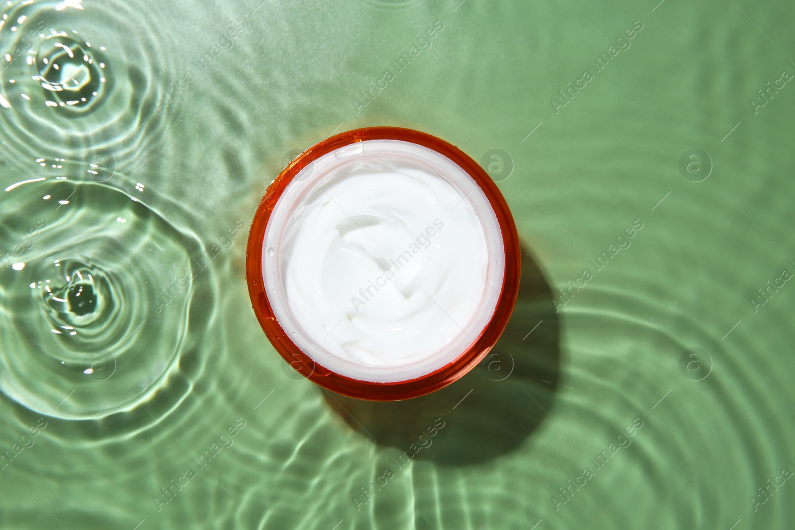 Photo of Jar with cream in water on light green background, top view. Cosmetic product