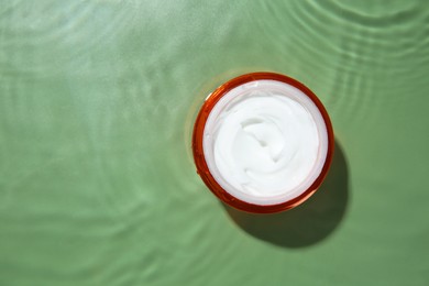 Photo of Cosmetic product. Jar with cream in water on light green background, top view. Space for text