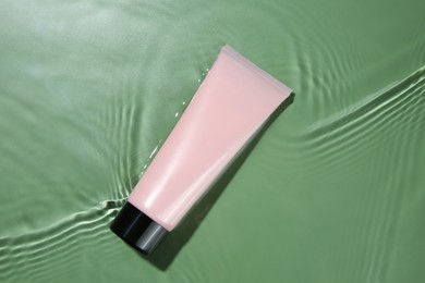 Photo of Tube with cream in water on light green background, top view. Cosmetic product