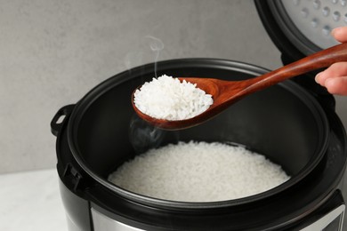 Photo of Woman taking boiled rice with wooden spoon on grey background, closeup