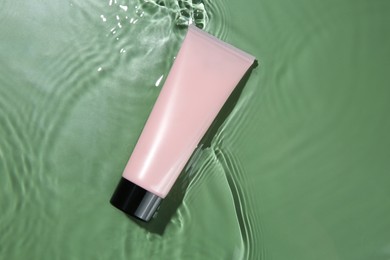 Tube with cream in water on light green background, top view. Cosmetic product