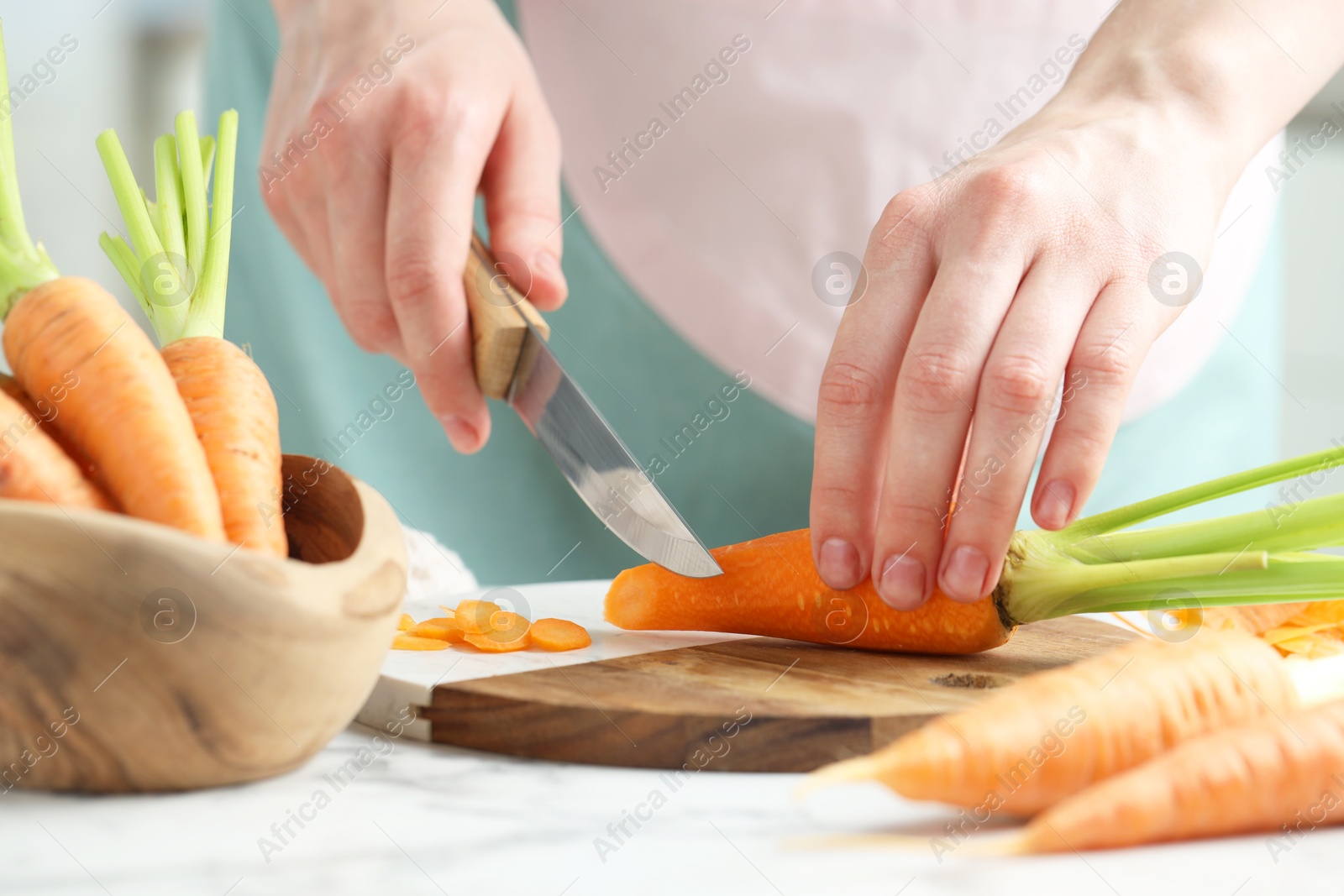 Photo of Woman cutting fresh carrot at white marble table, closeup