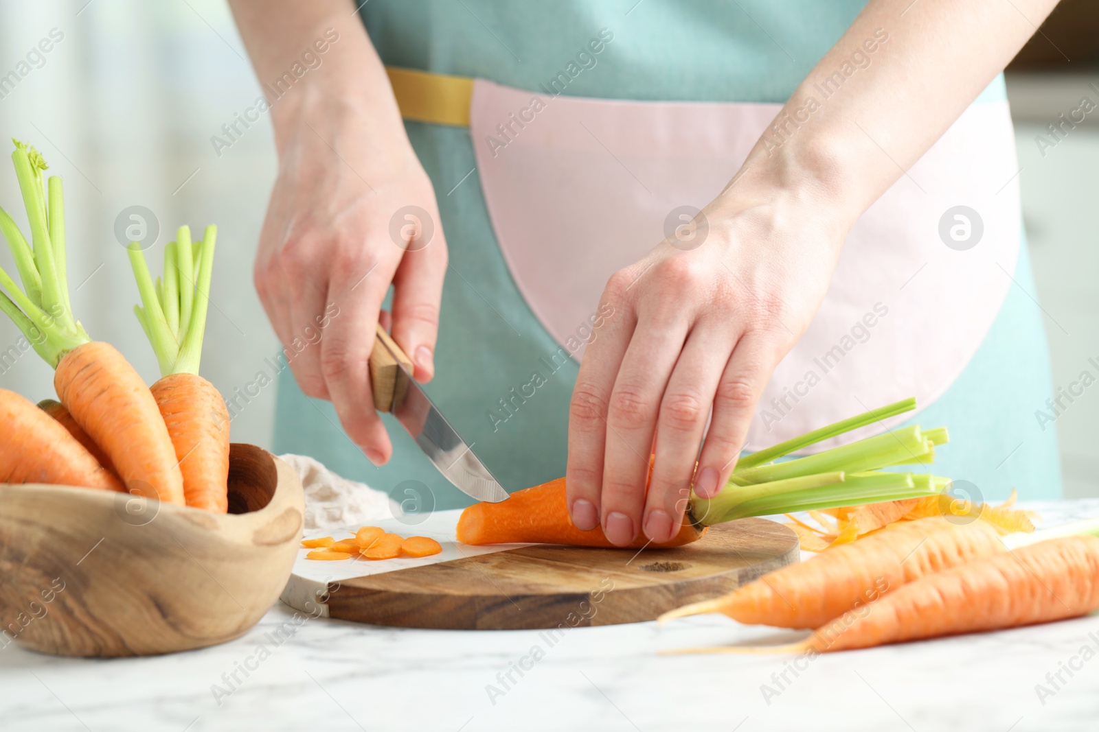 Photo of Woman cutting fresh carrot at white marble table, closeup