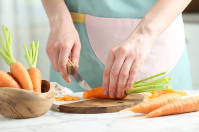 Photo of Woman cutting fresh carrot at white marble table, closeup