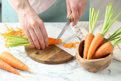 Photo of Woman cutting fresh carrot at white marble table, closeup